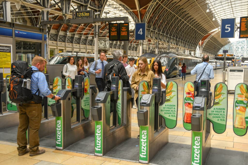 Rail travellers passing through automatic ticket barriers on the concourse at London Paddington railway station.