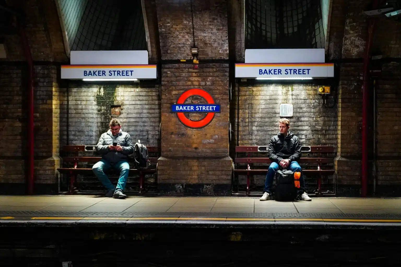 The London Night Tube — Saving Your Weekend Since 2016 Two people sitting on benches waiting for the Tube at Baker Street station.